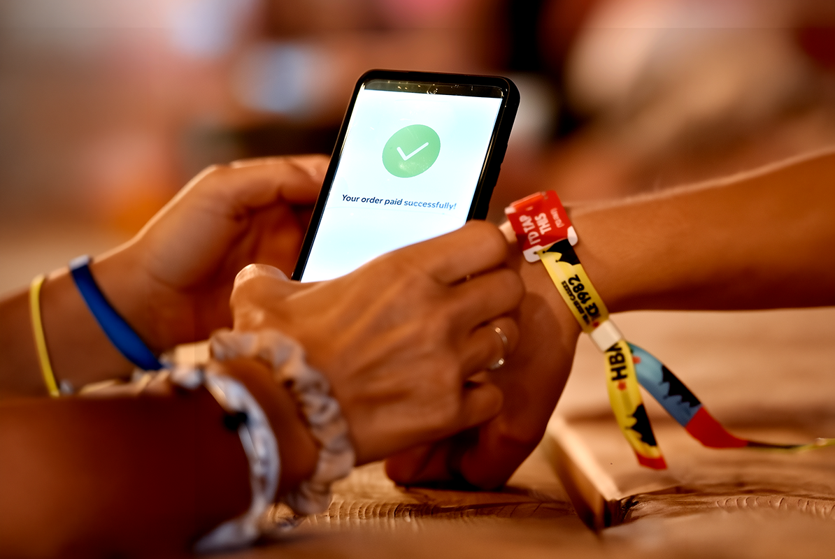 A guest tapping a wristband against a staff phone, with a paid confirmation on screen